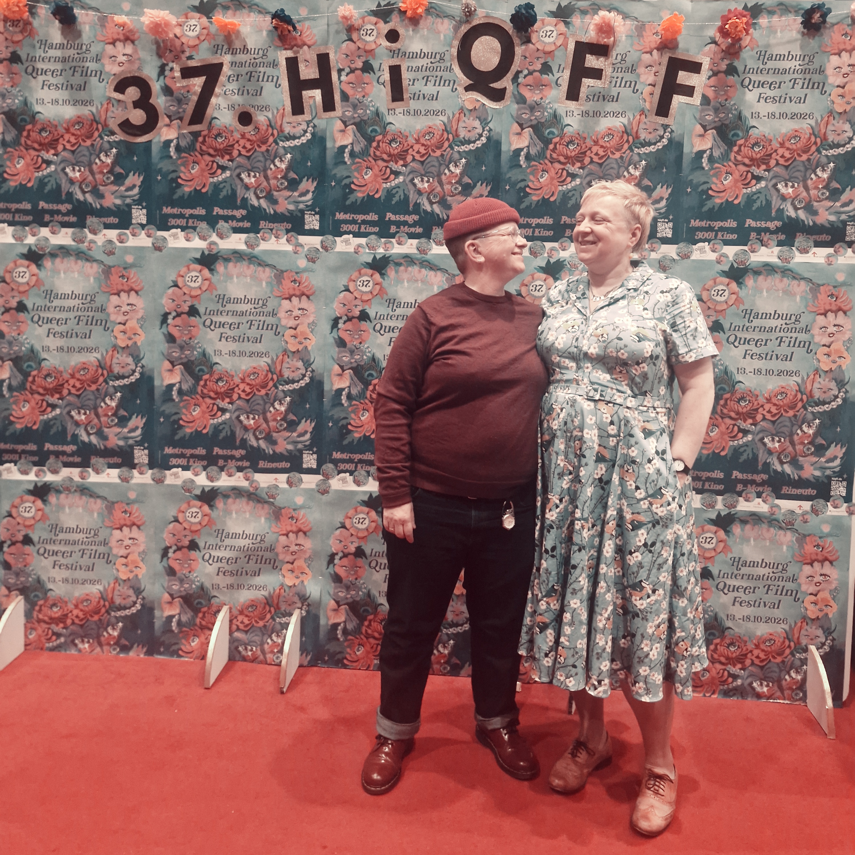 butch femme couple in front of signage for the queer film festival hamburg