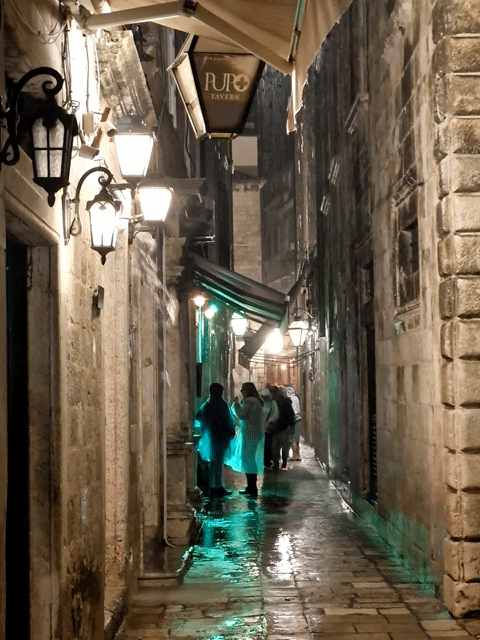 People sheltering under canvas roof outside a pub in an alley in Dubrovnik at night